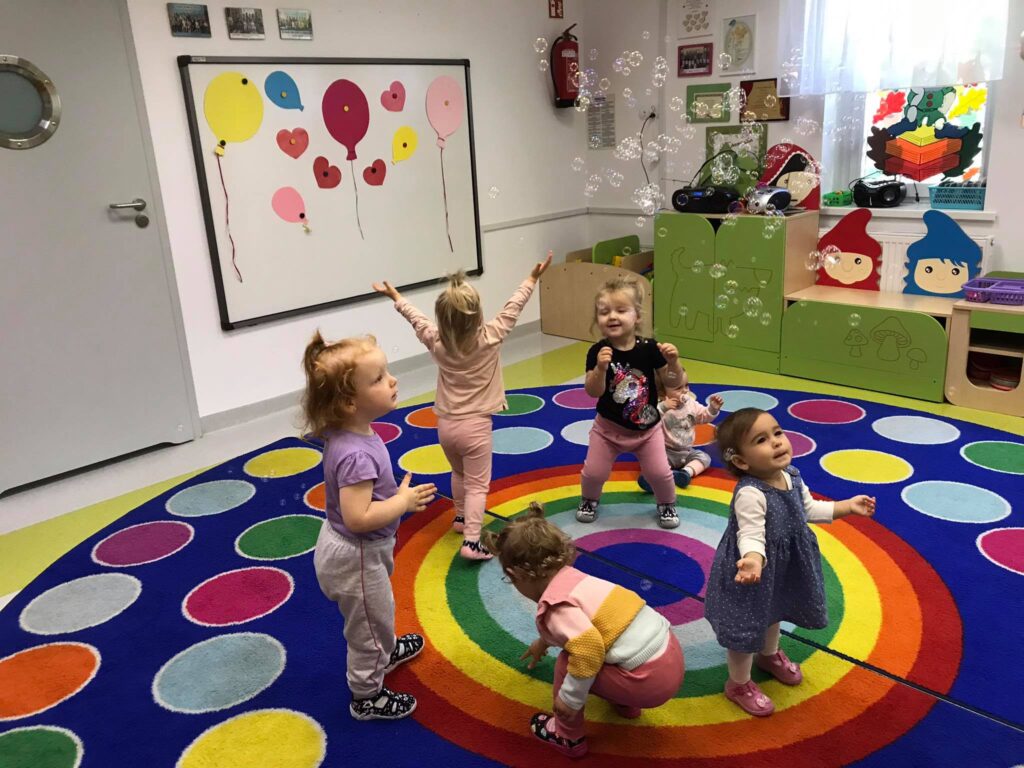 Grupa uśmiechniętych dzieci bawi się w sali bańkami mydlanymi