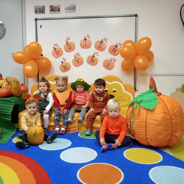 Dzieci z grupy Muchomorków uczestniczą w dniu dyni. Maluchy ubrane są na pomarańczowo oraz trzymają dynię.  