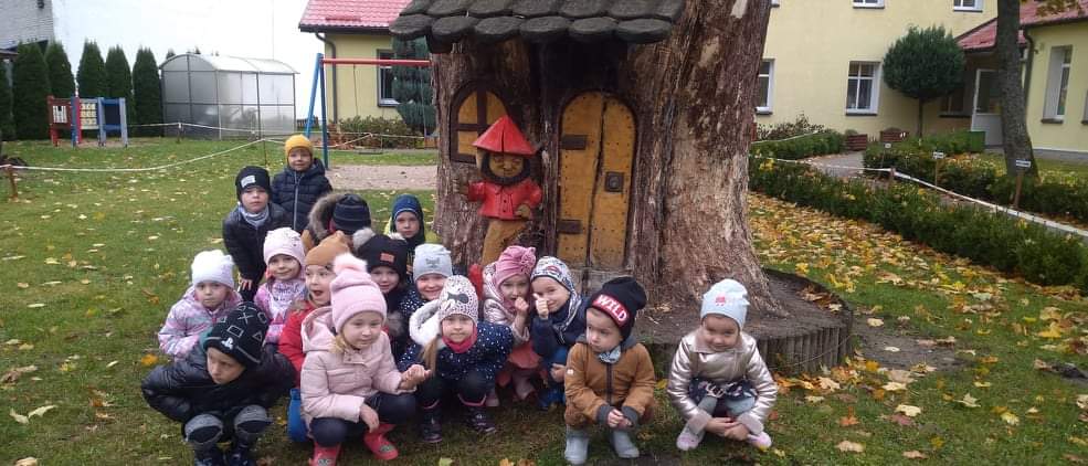 grupa dzieci pozuje do zdjęcia na tle rzeźby w pniu drzewa przedstawiającej Krasnala Hałabałę 