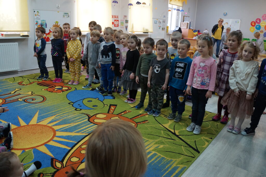 Dzieci z grupy II stoją w rzędzie przed maluszkami i śpiewają piosenkę z okazji pasowania na przedszkolaka