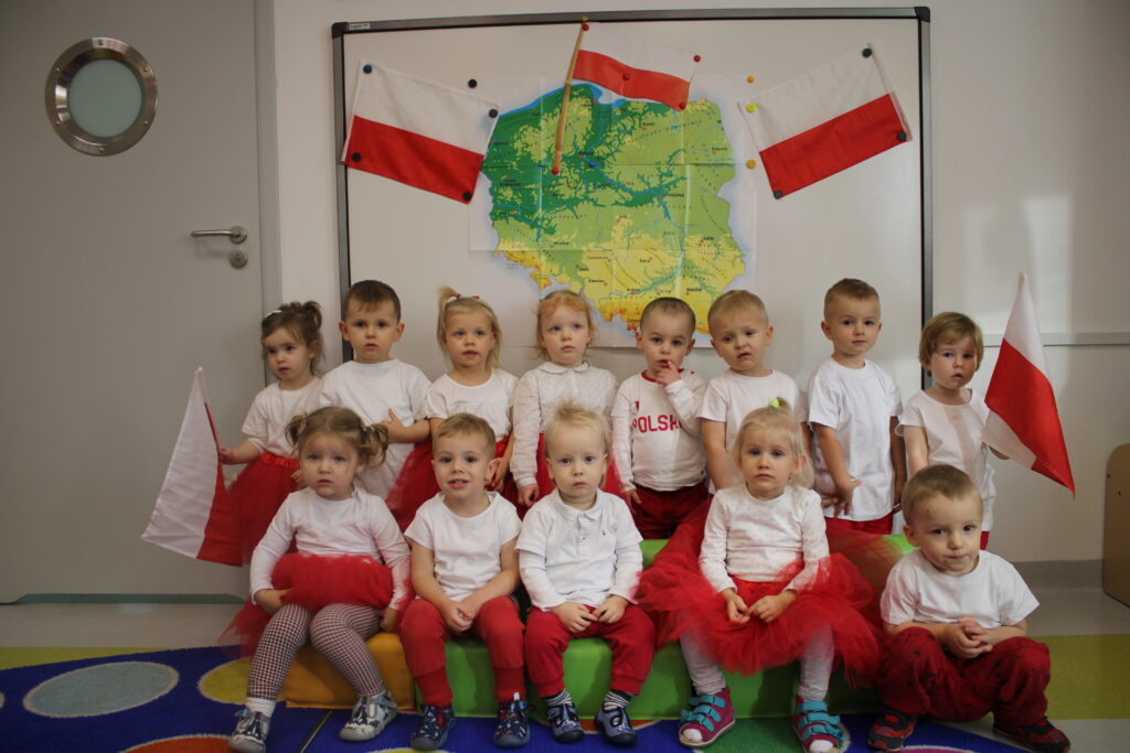 Dzieci starsze ze Żłobka prezentują Barwy Narodowe. w ręku trzymają flagi. 