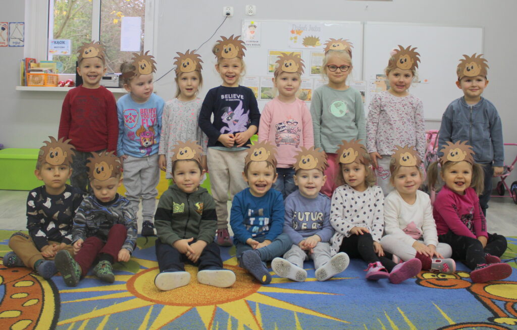 Dzieci obchodzą dzień jeża w przedszkolu. Mają opaski na głowach w kształcie głowy jeża. Uśmiechają się do zdjęcia.
