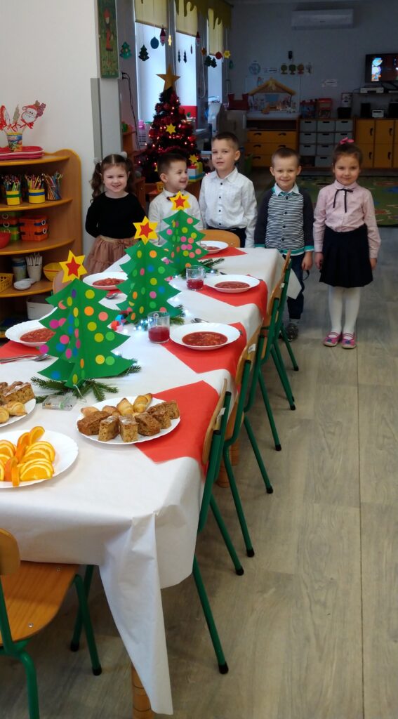 Pięcioro dzieci z grupy II stoi przy świątecznie zastawionym stole, tuż przed uroczystym obiadem