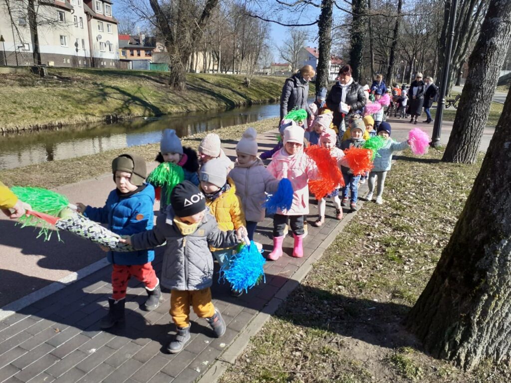 Grupa maluchów z pomponami w dłoni idzie na spacer aby przywitać wiosnę.