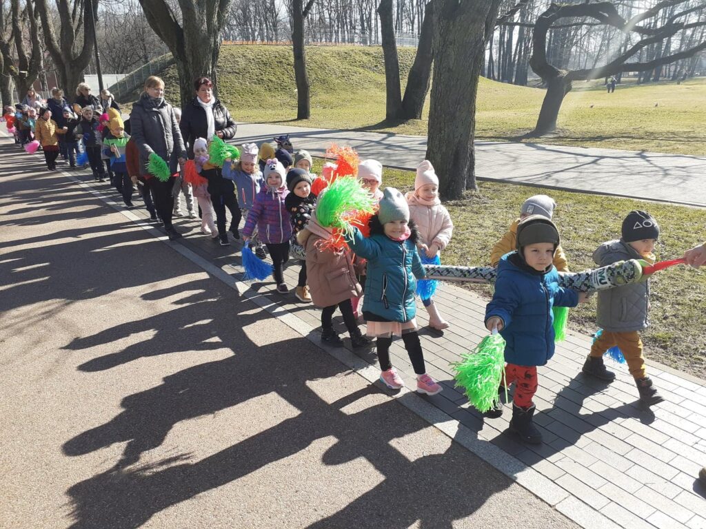 Grupa maluchów z pomponami w dłoni idzie na spacer aby przywitać wiosnę.