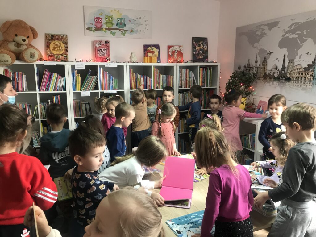 Dzieci zwiedzaja bibliotkę. Oglądaja wybrane pozycje ksiązkowe w sali dla namłodszych czytelników. 