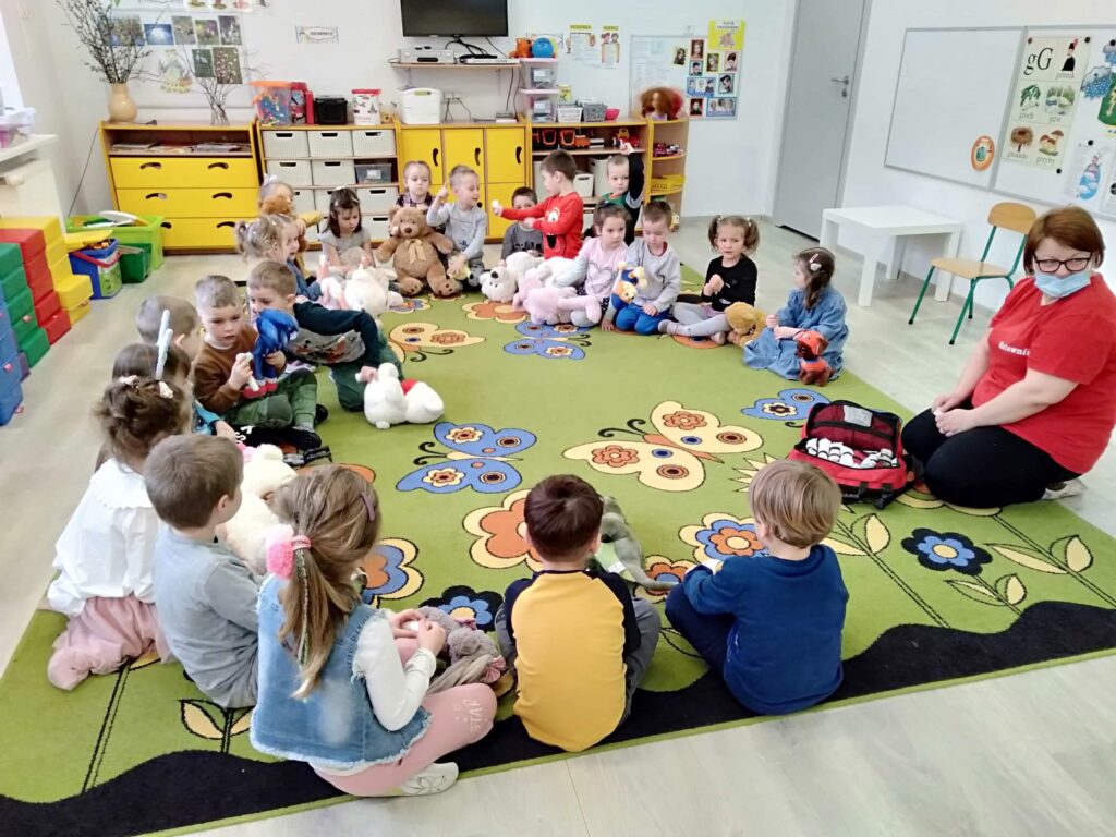 Dzieci w przedszkolu siedza na dywanie w kole. Każdy przedszkolak trzyma w ręku swojego ulubionego pluszaka. zaproszony gość- pani ratownik pokazuje swoją apteczkę i opowiada o swojej pracy i o tym jak udzielac pierwszej pomocy.