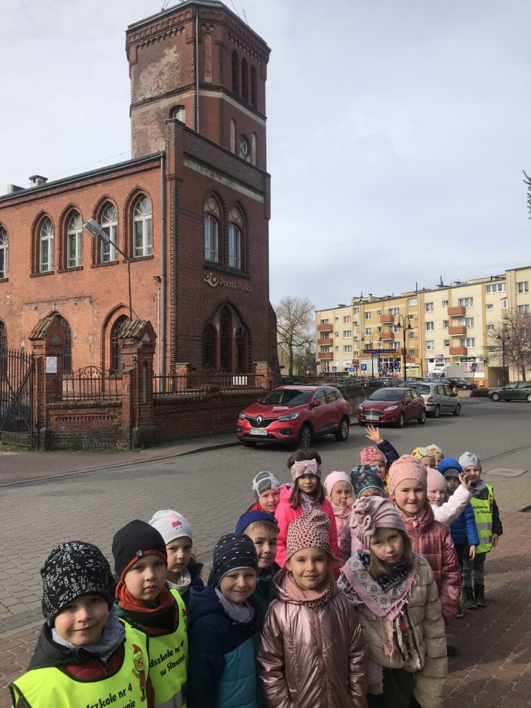 Nasze przedszkolaki  zwiedzają miasto Sławno. Stoją przed budynkiem zabytkowej poczty.