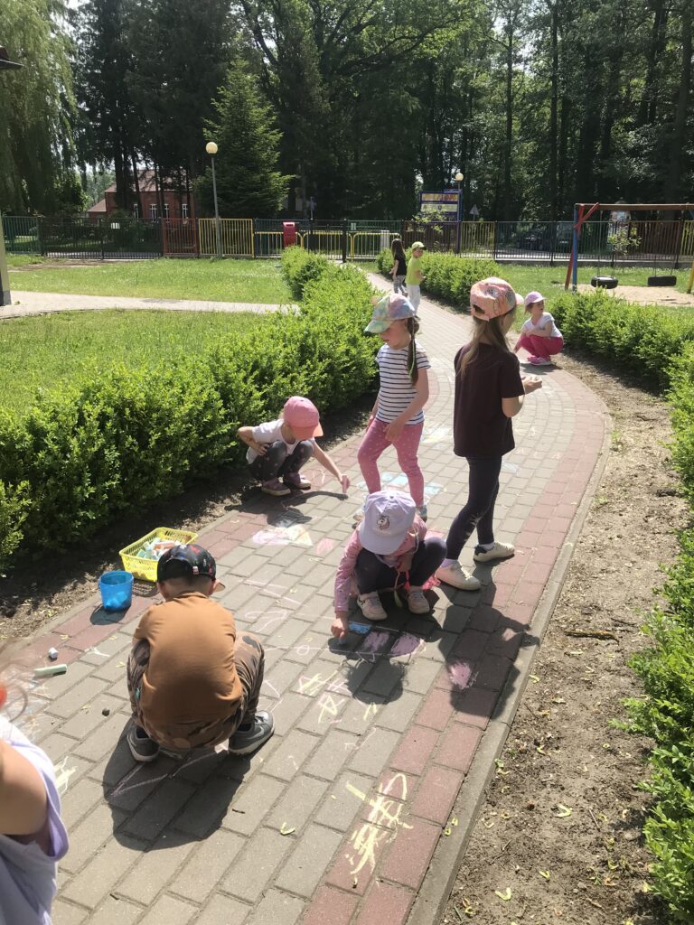 Dzieci bawią się w ogrodzie , rysują kolorową kredą na chodniku. 