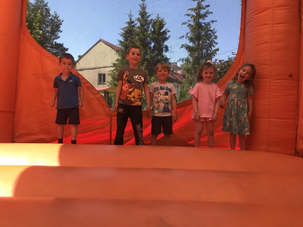 Dzieci przedszkole- 5 osób stoi w środku wielkiego dmuchanego tygryska. Przedszkolaki skaczą na dmuchańcu w piękny letni dzień. 