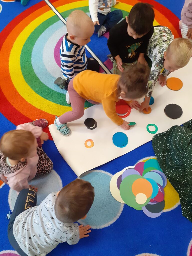 Grupa dzieci wykonuje zadania - dopasowuje kropkę według koloru na arkuszu papieru.