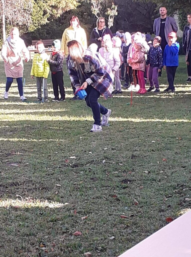 Zdjęcie pzredstawia sportowa zabawę-wyścicg z ziemnakami, w czasie święta pzredszkolnego. W zabawie uczestnicza rodzice i dzieci.