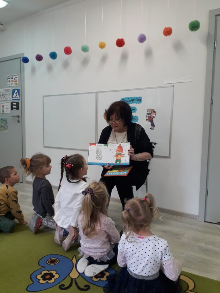 Pani Bogusia z Miejskiej Biblioteki w Sławnie pokazuje dzieciom z grupy drugiej ilustracje w książce.