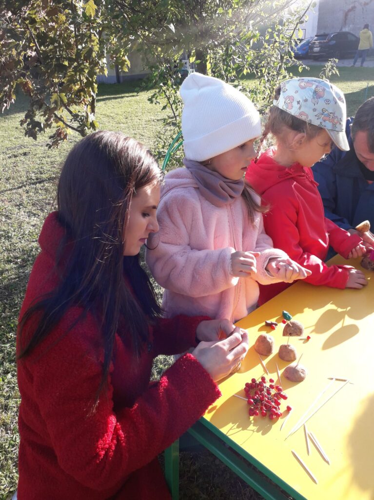 Dzieci i rodzice konstruują ludziki z ziemniaków przy stoliku.