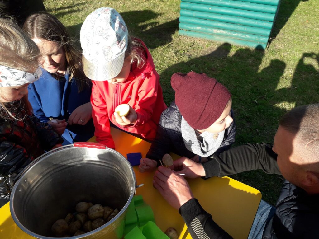 Dzieci i rodzice przy stoliku konstruują ludziki z ziemniaków.