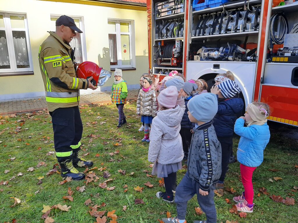dzieci oglądają sprzęt strażacki . na zdjęciu strażak prezentuje kask