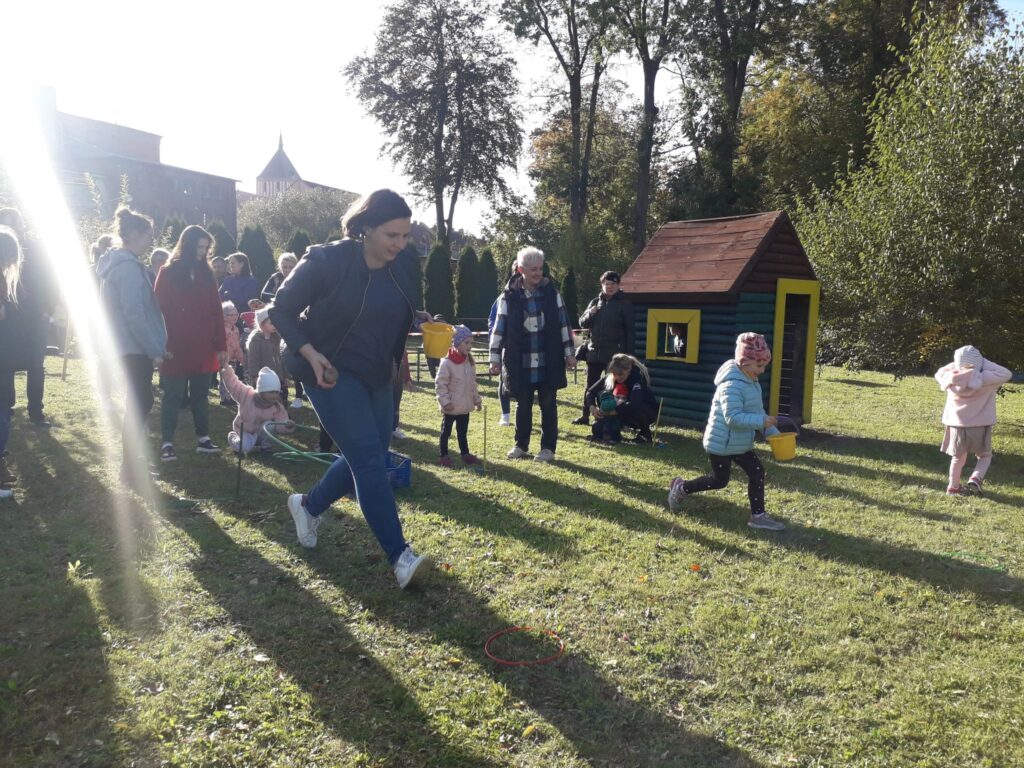 Mama z córką rywalizuje w konkurencji sadzenia ziemniaków. W tle pozostali uczestnicy zawodów. 