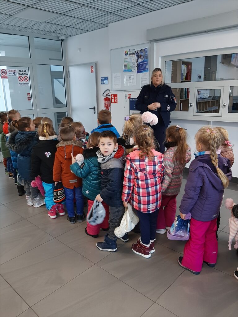 Grupa dzieci wraz z panią policjantką stoją w pomieszczeniu Komendy policji w Sławnie.