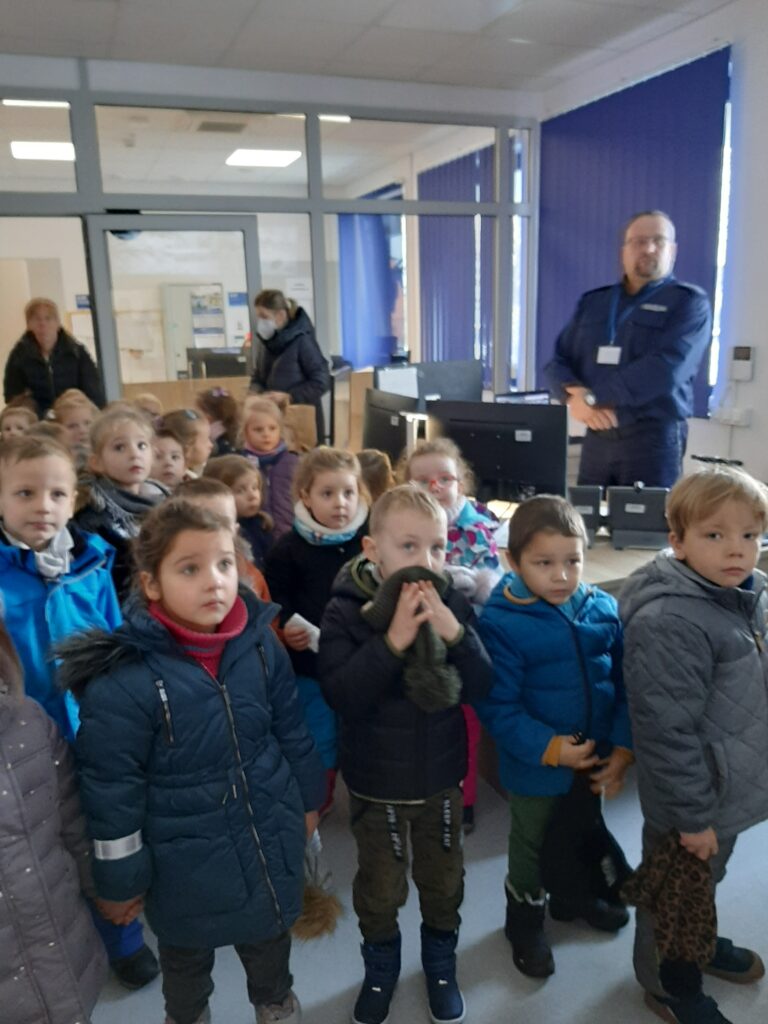 Pan policjant pełniący służbę w dyżurce Komendy miejskiej w Sławnie objaśnia dzieciom stojącym przed nim, co widzą na monitorach z kamer miejskich.