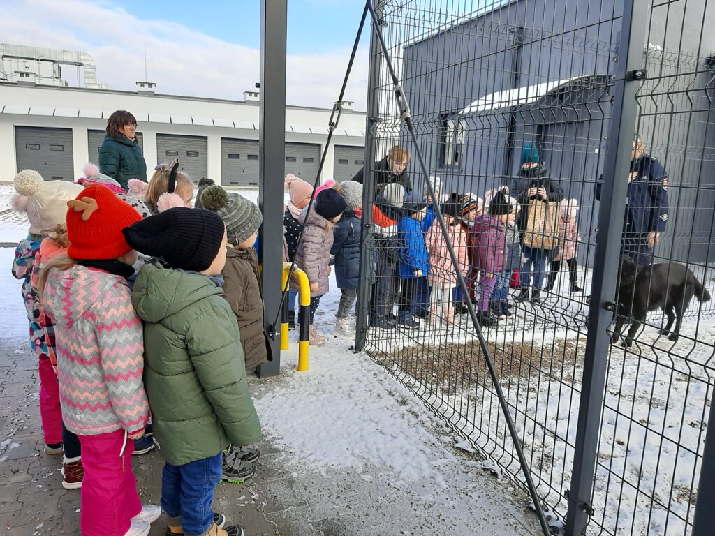 Dzieci , panie i pani policjantka obserwują psa Nero w kojcu.