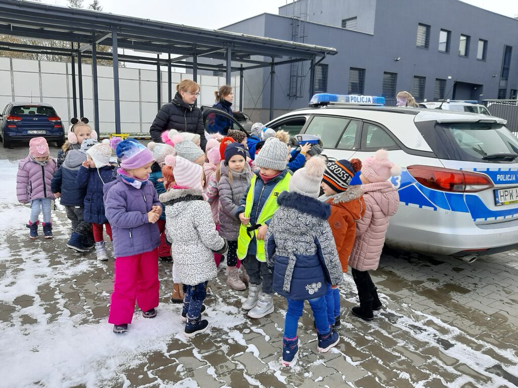 Grupa dzieci, pani i panie policjantki stoją przy radiowozie policyjnym.