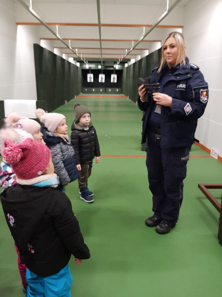 Pani policjantka pokazuje dzieciom pistolet treningowy.