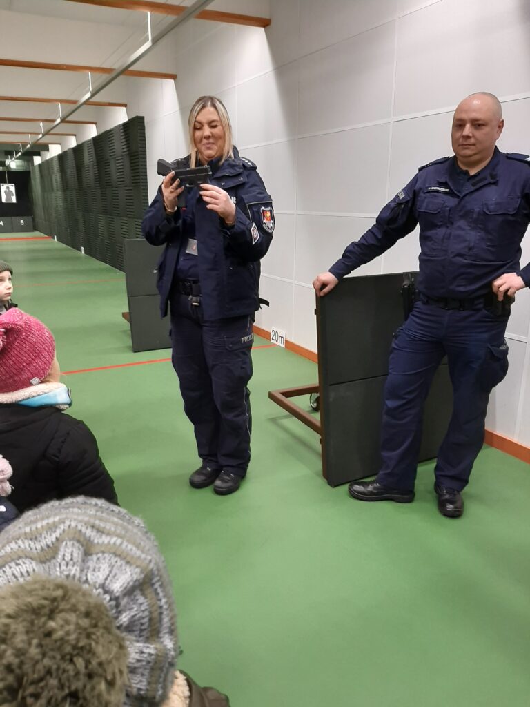 Dwoje policjantów opowiada dzieciom o zasadach bezpieczeństwa podczas treningu strzeleckiego.