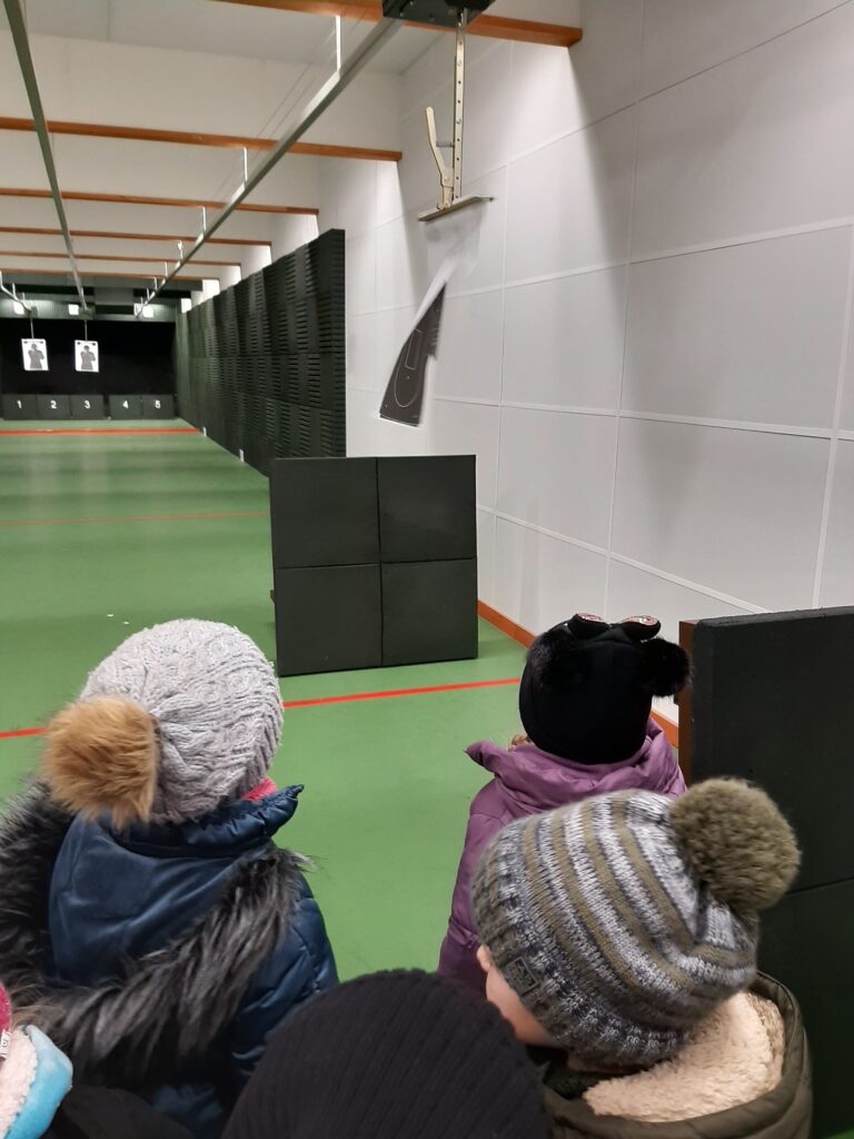 Dzieci obserwują przejazd tarczy strzelniczej po szynie w pomieszczeniu strzelnicy Komendy Policji w Sławnie.