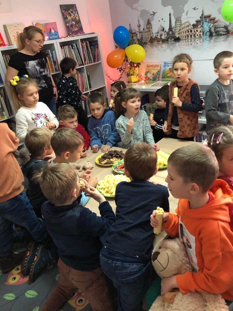 Przedszkolaki zjadają słodkości przygotowane dla nich z okazji święta Misia w bibliotece miejskiej.