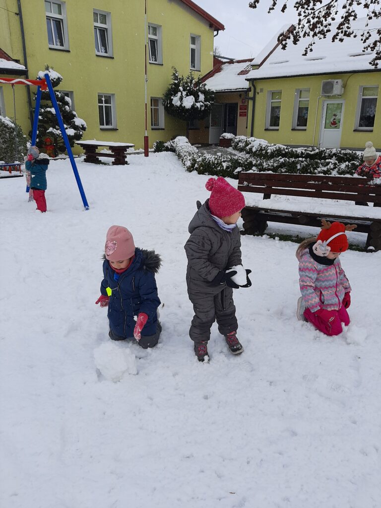 Kilkoro dzieci bawi się na śniegu w przedszkolnym ogrodzie.