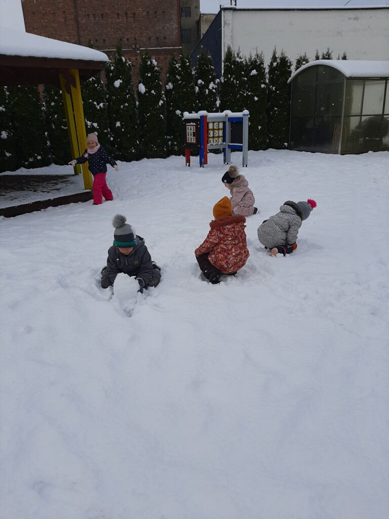 Dzieci bawią się na śniegu w przedszkolnym ogrodzie.