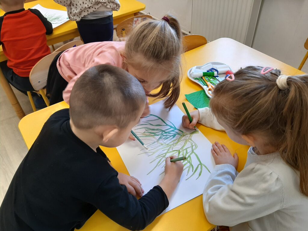 Troje dzieci koloruje kredkami gałązkę jemioły.