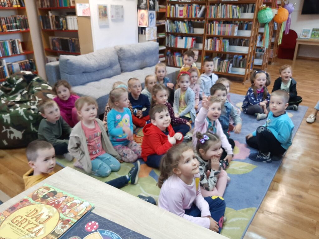 DZIECI SŁUCHAJĄ BAJKI CZYTANEJ PRZEZ PANIĄ BIBLIOTEKARKĘ