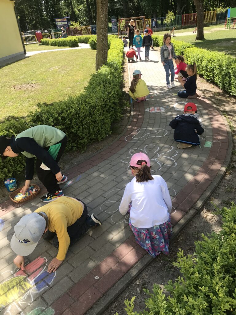 Dzieci rysują kolorowe obrazki na chodniku przed swoim przedszkolem.