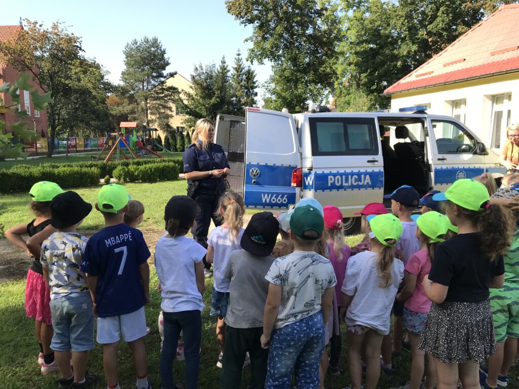 Spotkanie z ppolicjantka w przedszkolnym ogrodzie. Dzieci stoja i rozmawaiaja na temat bezpieczeństwa, 