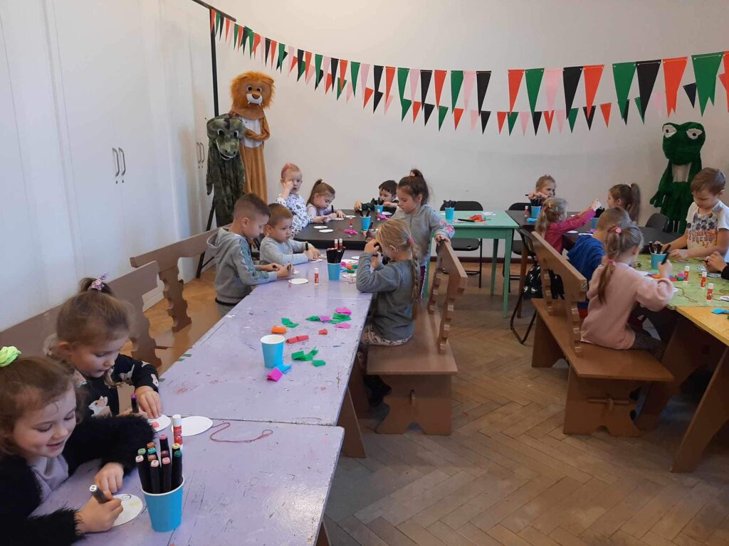 Dzieci z najstarszej grupy po seansie filmowym w SDK uczestnicza w warsztatach plastycznych. Siedza w sali i rysuja medaliony. 