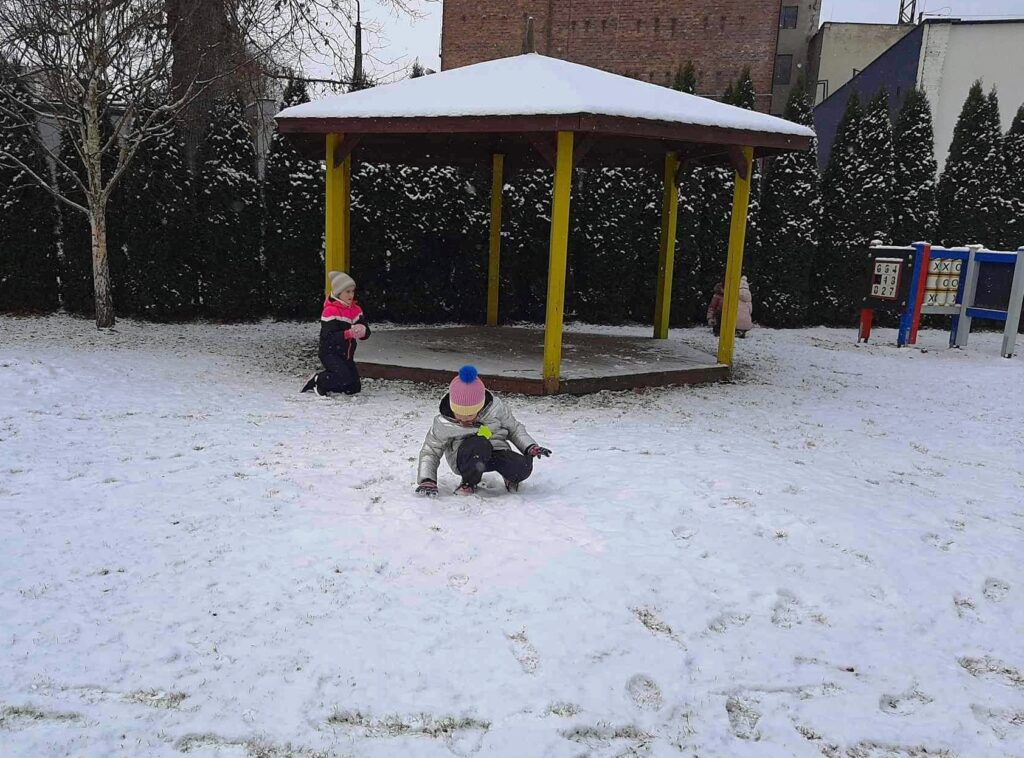 Radość dzieci, bo spadł pierwszy śnieg. Bawią się w pzredszkolnym ogrodzie