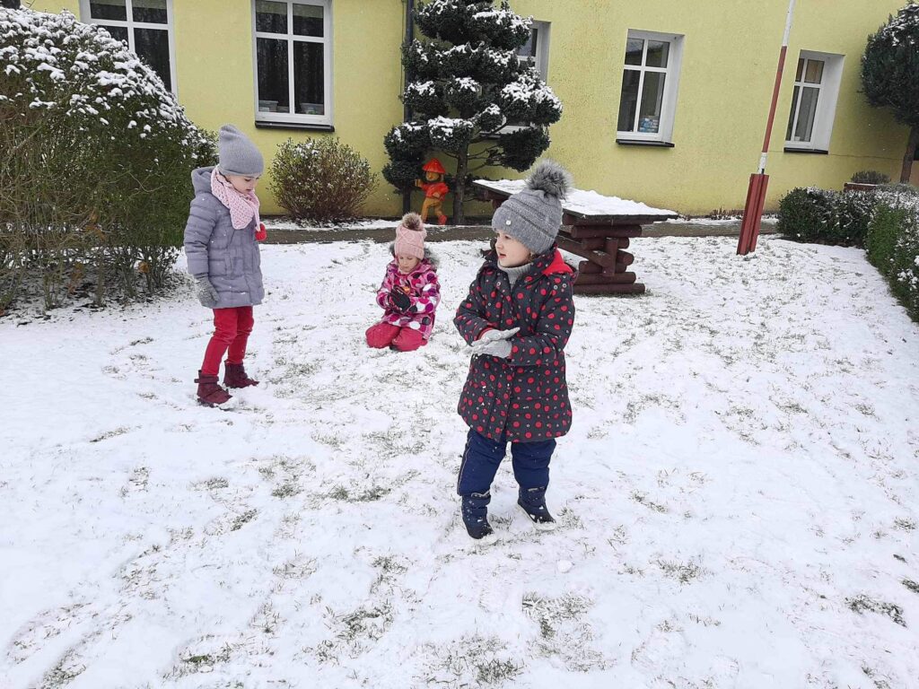 Dziewczynki bawią się śniegiem który spadł w przedszkolnym ogrodzie po raz pierwszy w tym roku