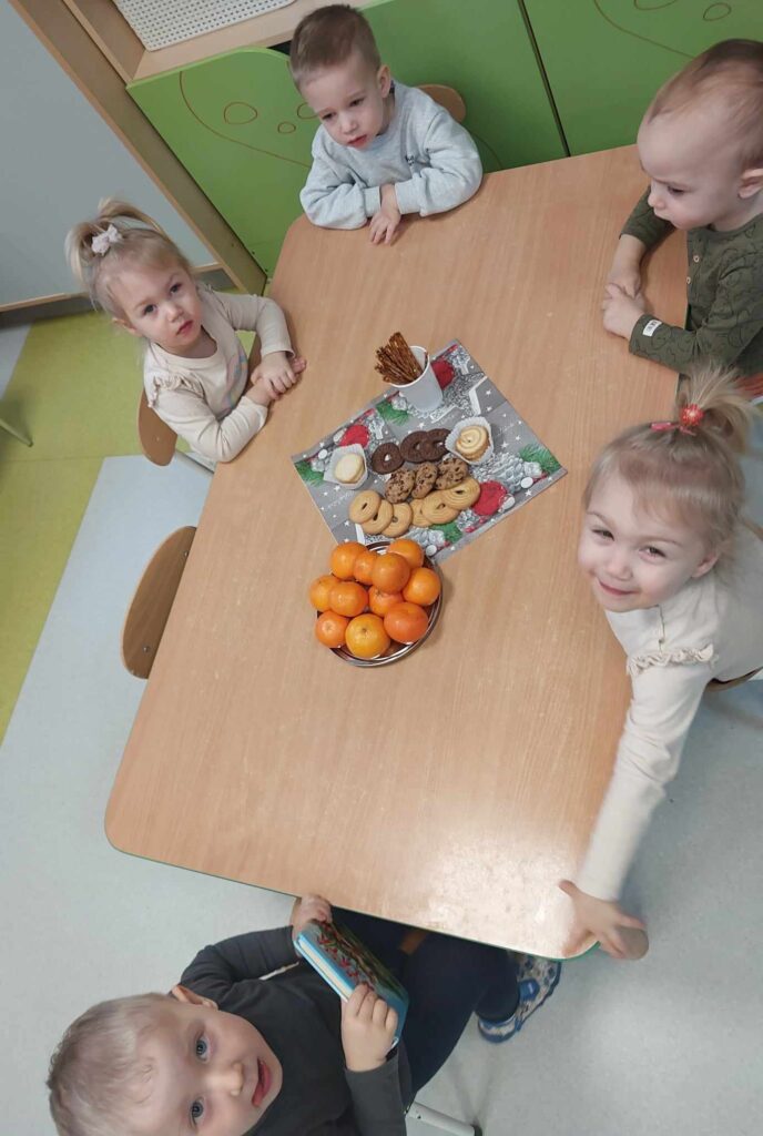 Dzieci siedząc przy stoliku częstują się słodkościami.