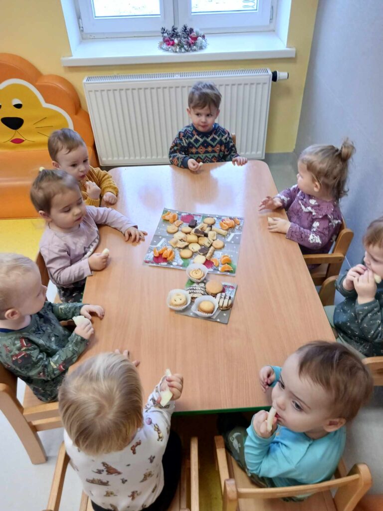 Dzieci siedząc przy stoliku częstują się słodkościami.