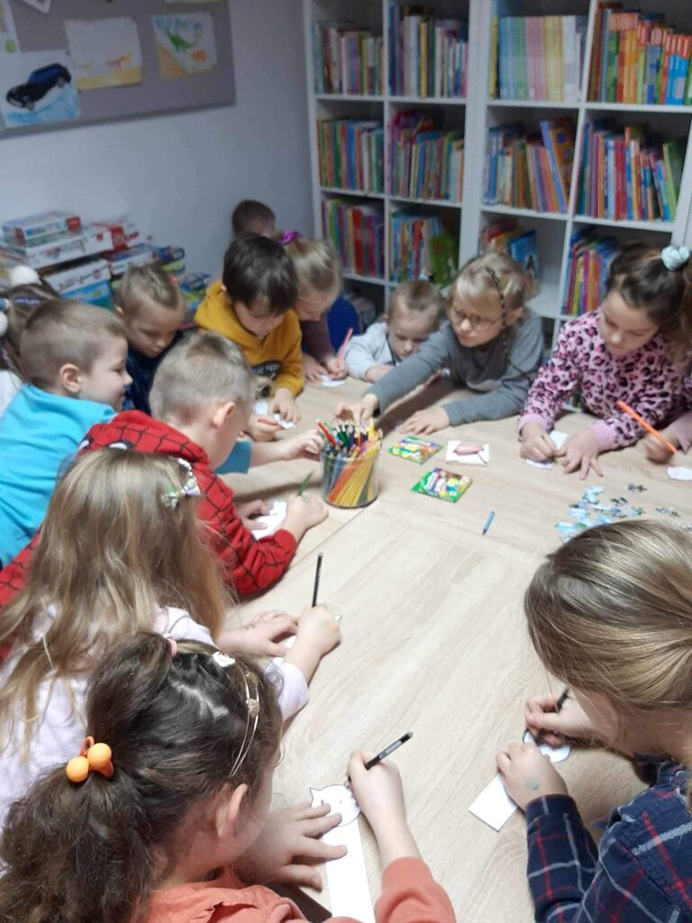 dzieci na zajeciach w bibliotece wykonuja zakladki w ksztacie kota , koloruja kredkami. 