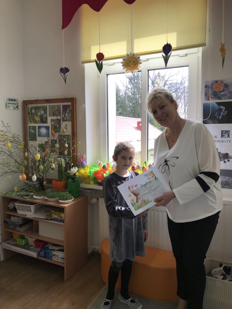 Hania otrzymuje dyplom wręczany przez dyrektora przedszkola za udział w konkursie plastycznym 