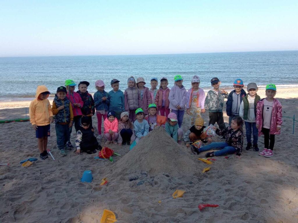 DZIECI POZUJĄ DO ZDJĘCIA NA PLAŻY W JAROSŁAWCU PRZY ZAMKU Z PIASKU