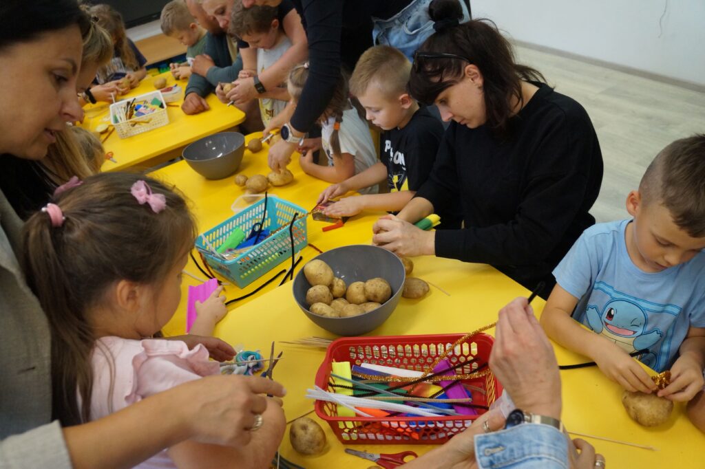 Rodzice wraz z dziećmi tworzą pracę plastyczną.