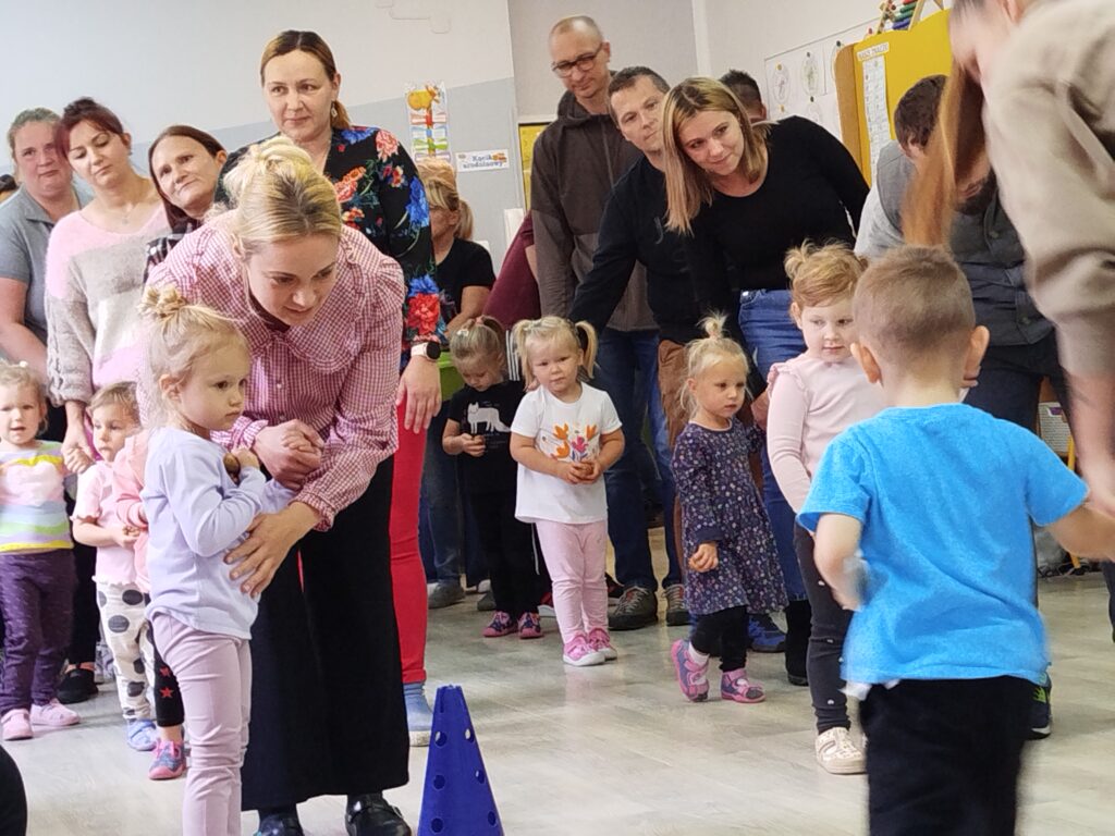 rodzice wraz z dziećmi biorą udział w konkurencjach z ziemniakiem. dziewczynka podnosi ziemniaka z krążka