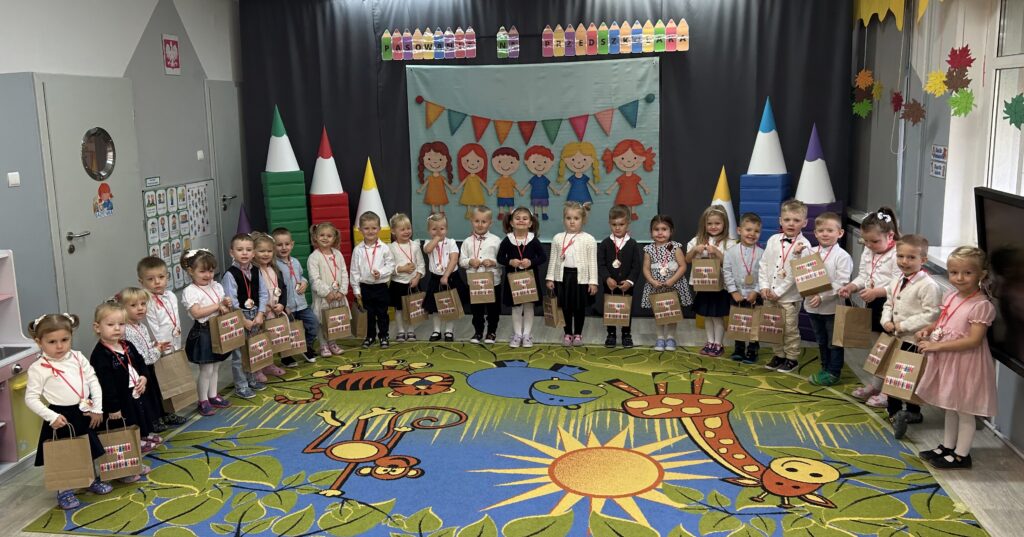 W czasie uroczystości PASOWANIA NA PRZEDSZKOLAKA dzieci stoją w półkolu, na szyji mają medale w rękach trzymają upominki