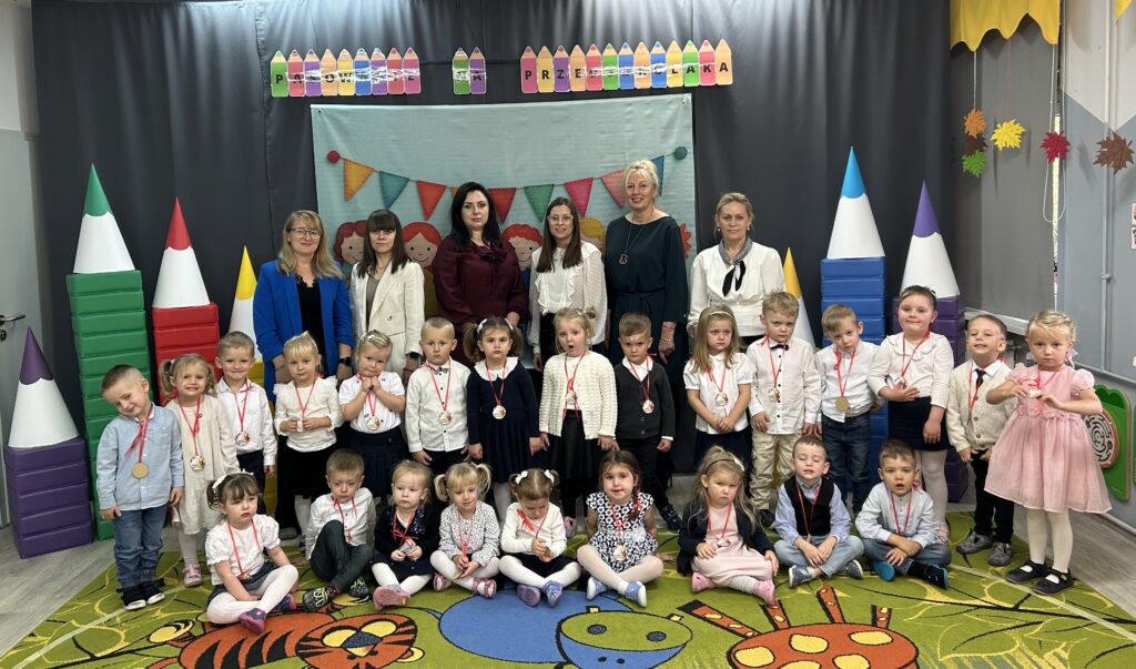 Pamiątkowe zdjęcie po uroczystości pasowania na przedszkolaka. Dzieci stoją przed dekoracją razem ze swoimi Paniami pracującymi w grupie.