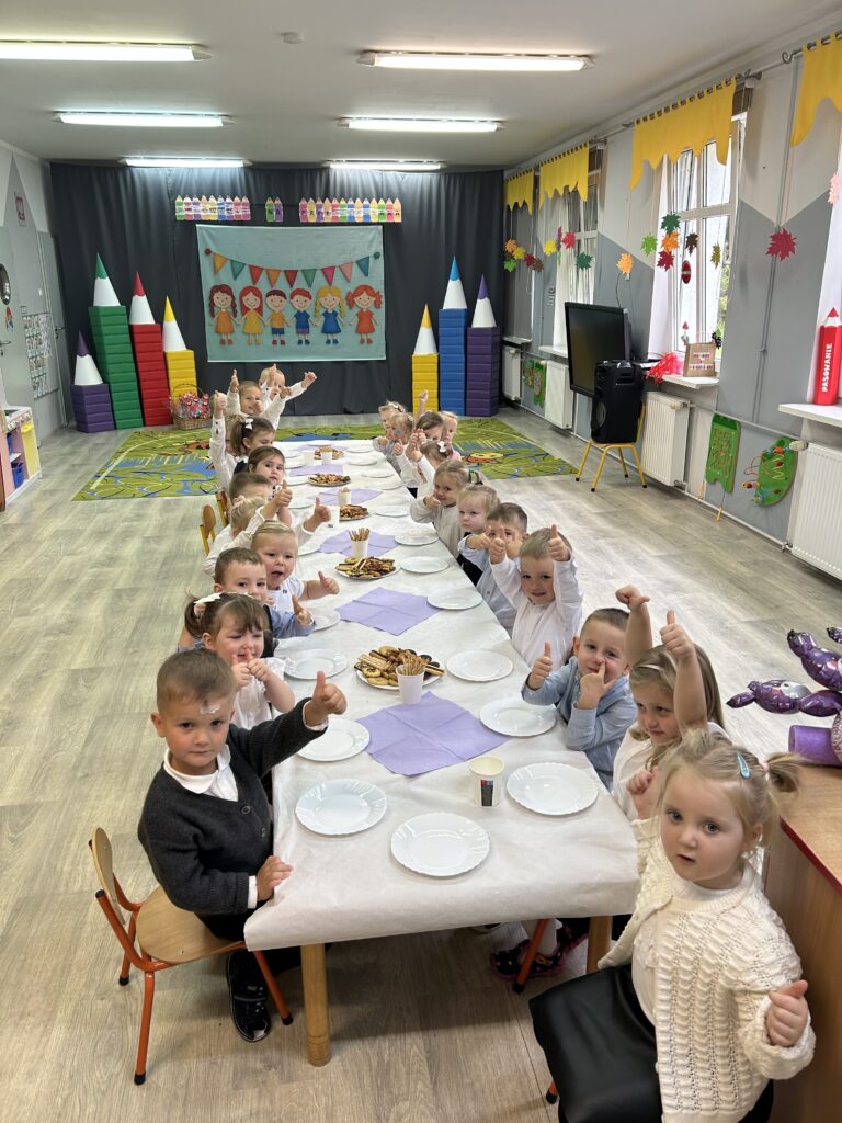 Poczestunek z okazji święta w przedszkolu- pasowania na przedszkolaka. dzieci siedzą [przy stołach , będą zjadały slodkości przygotowane z tej okazji. 