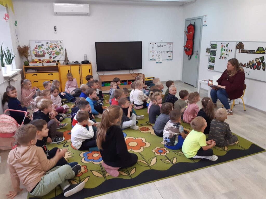 DZIECI SŁUCHAJĄ BAJKI CZYTANEJ PRZEZ PRACOWNIKA BIBLIOTEKI MIEJSKIEJ W SŁAWNIE