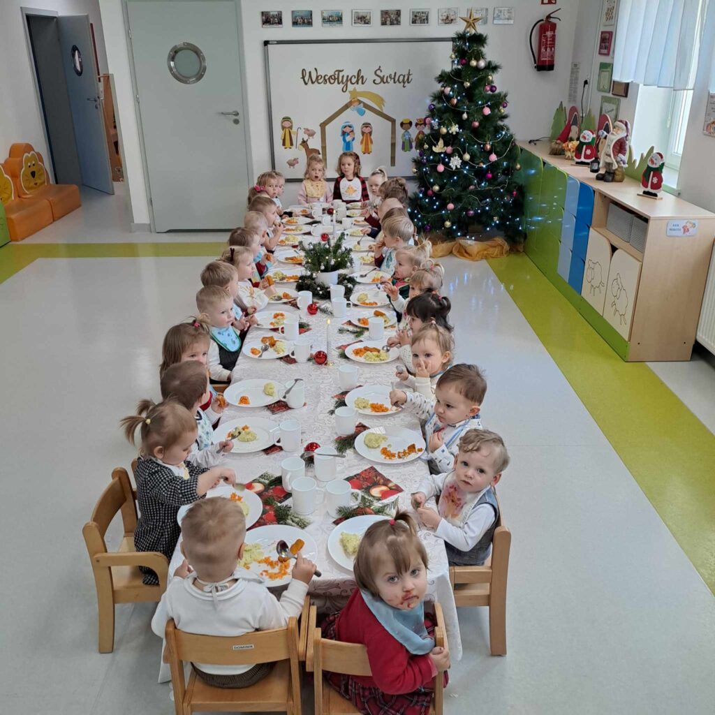 DZIECI JEDZĄ ŚWIĄTECZNY POSIŁEK PRZY WSPÓLNYM STOLE
